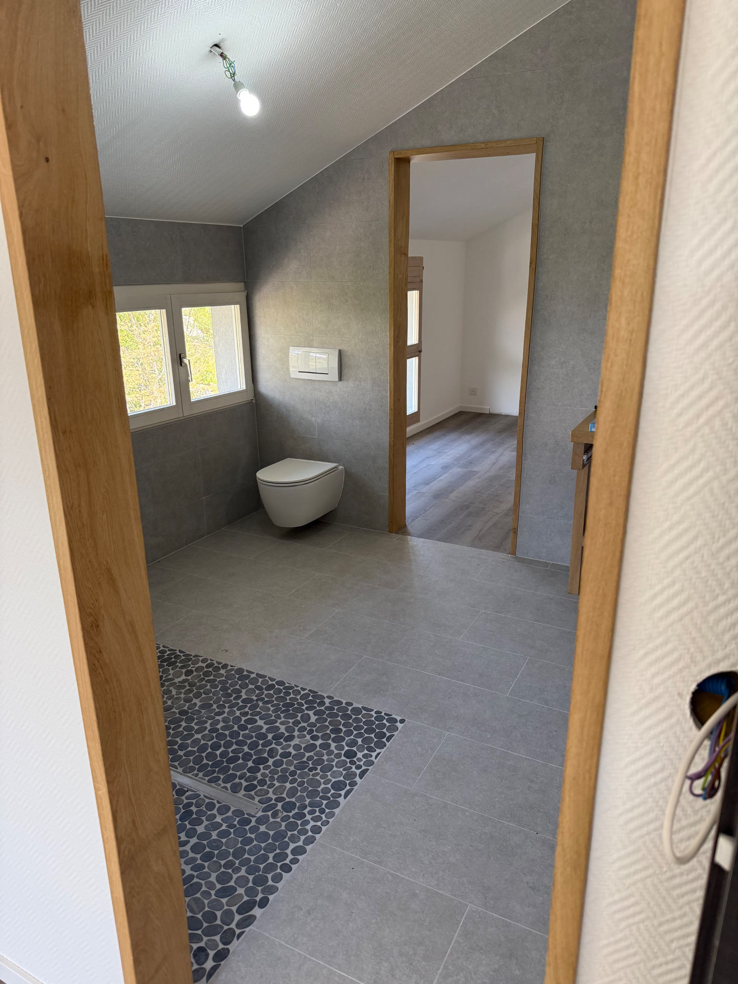 Espace sanitaire rénové avec WC suspendu, douche ouverte et carrelage gris