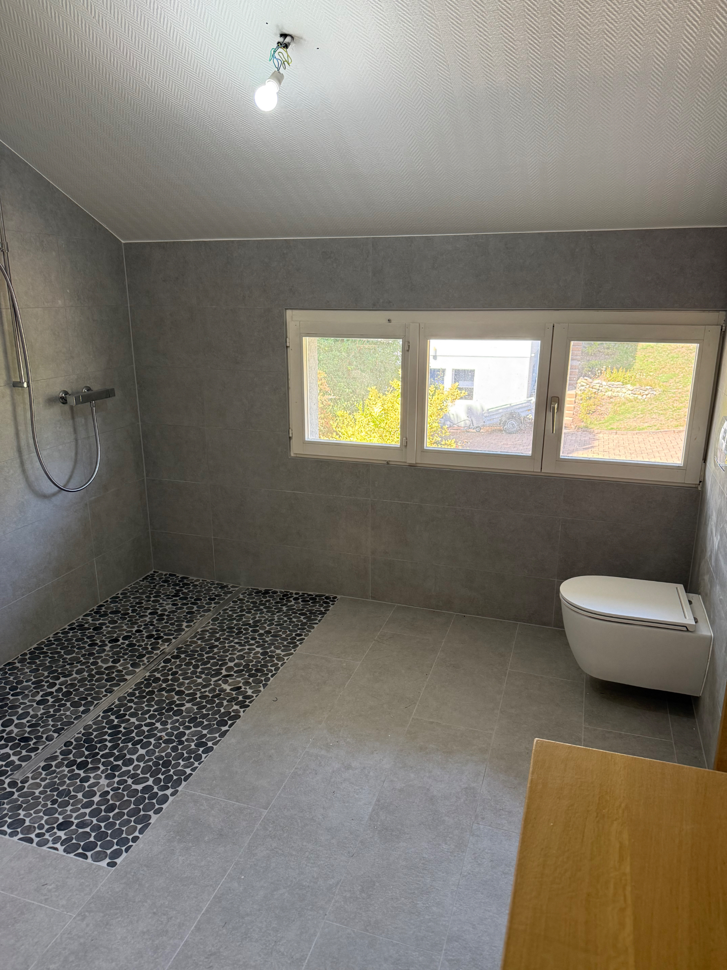 Grande douche ouverte rénovée avec galets noirs et carrelage gris