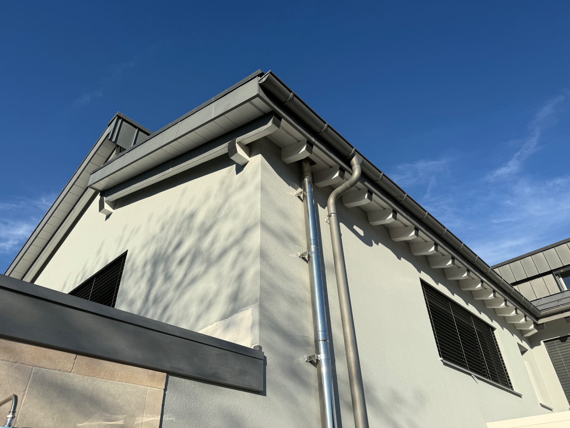 Façade moderne gris clair avec avant-toits repeints en blanc et chevrons blancs