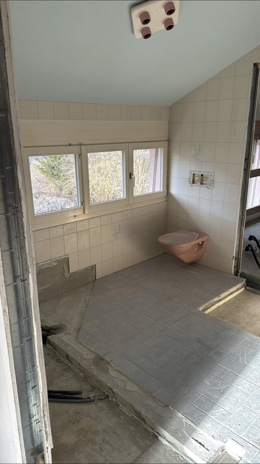 Ancienne salle de bain avec carrelage beige et WC rose avant rénovation