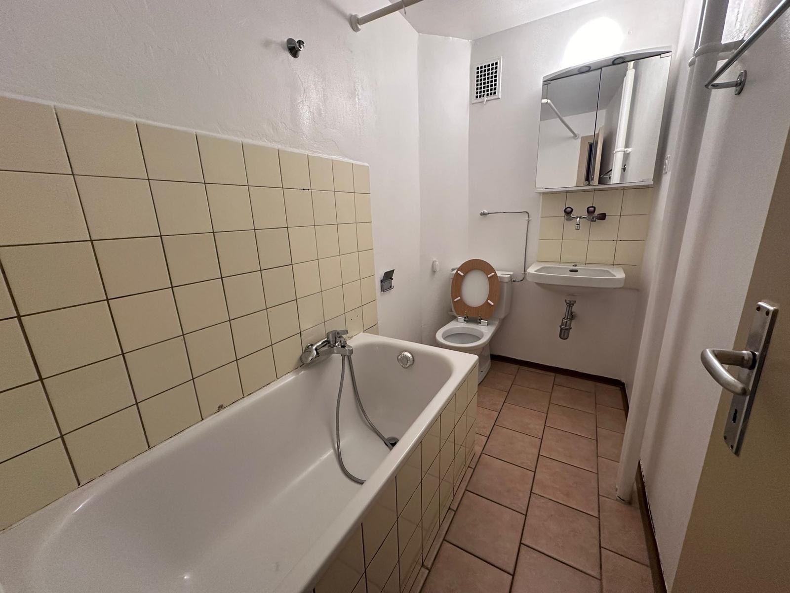 Salle de bain avant travaux : carrelage beige, baignoire et sanitaires d'origine