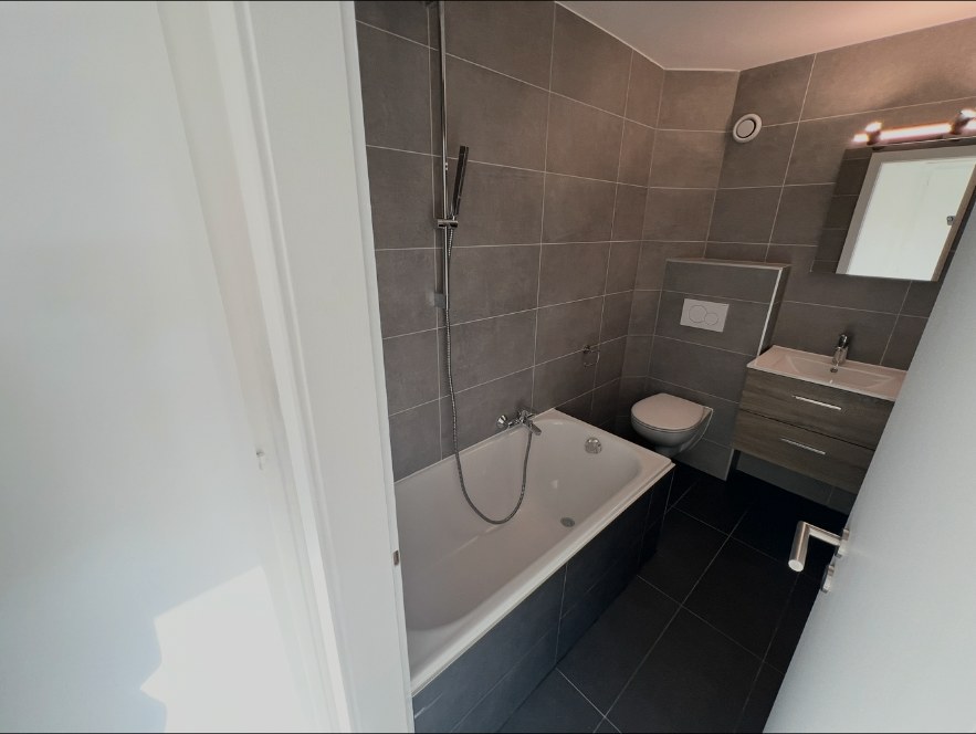 Salle de bain après travaux avec faïence grise, baignoire et meuble vasque