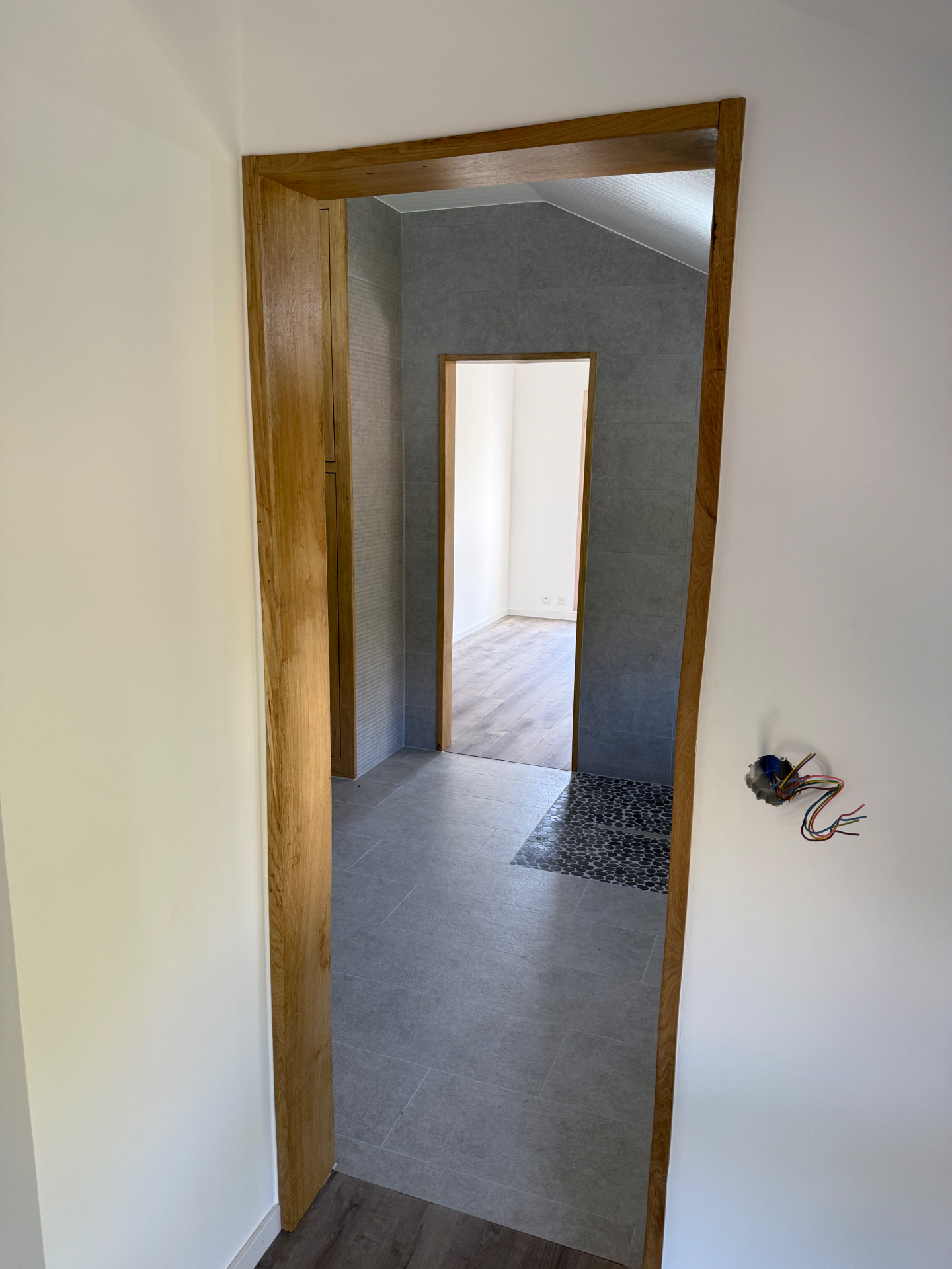 Salle de bain rénovée vue depuis l'entrée avec carrelage gris et encadrements en bois